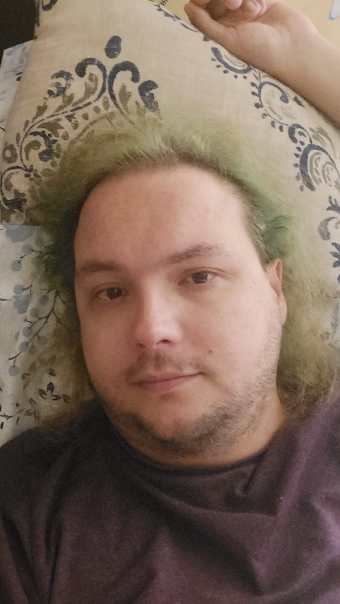 A man with long green hair wears pajamas while laying in bed, photo 1